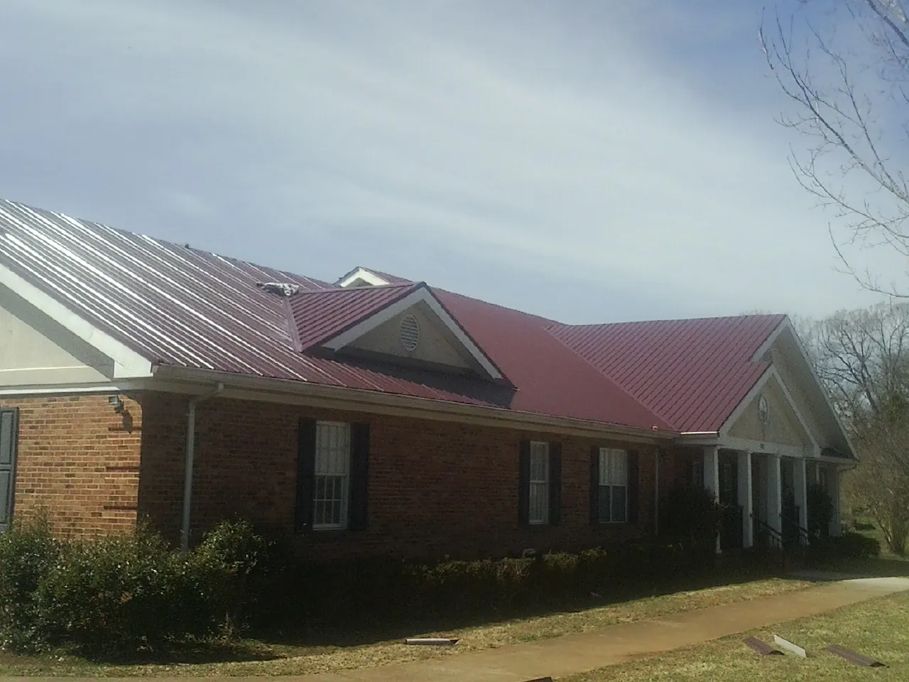 Red metal roof with gabled entries on a long brick building, from a Hail Damage Roof Repair job in Albion
